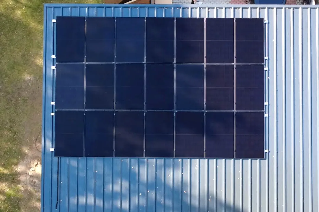 Luftaufnahme eines blauen Trapezblechdachs mit drei Reihen schwarzer Solarmodule